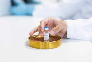 A NorthX employee placing a labeled vial on a gold-colored tray in a laboratory setting.